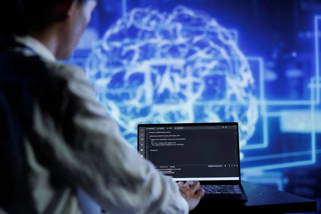 Persona programando en un portátil ante una visualización digital de inteligencia artificial